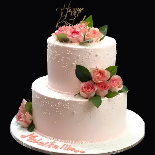 Light pink two-tier cake decorated with pink roses, green leaves, and shimmering sugar pearls