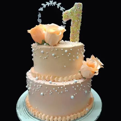 Light pink two-tier birthday cake with roses, silver pearls, and green leaves