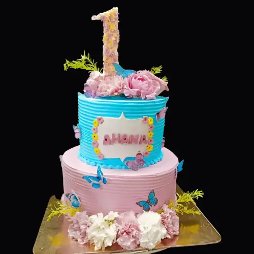 Blue and pink two-tier cake adorned with pink and white flowers, edible butterflies, and small fondant blooms