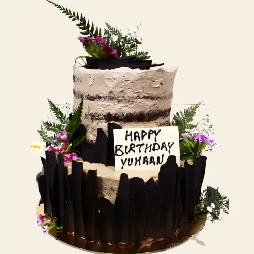 Rustic two-tier naked cake with fresh flowers, green leaves, and chocolate sticks